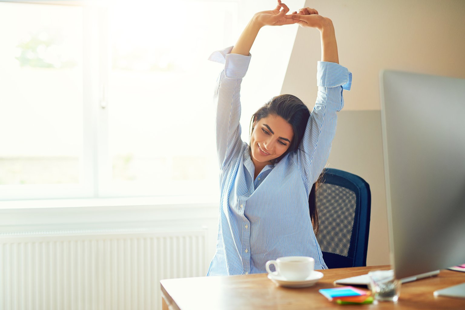 A woman stretching beside her desk at home during a work break