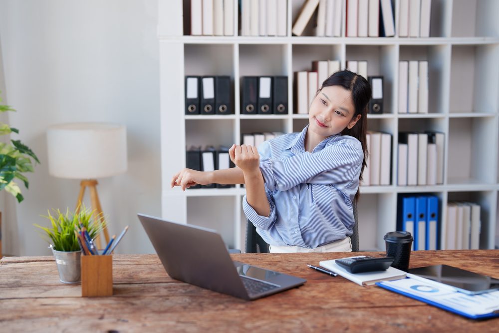 A woman stretching her arms and shoulders during a break from her desk