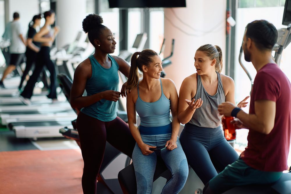 A group of gym members chatting and taking a break together between sets