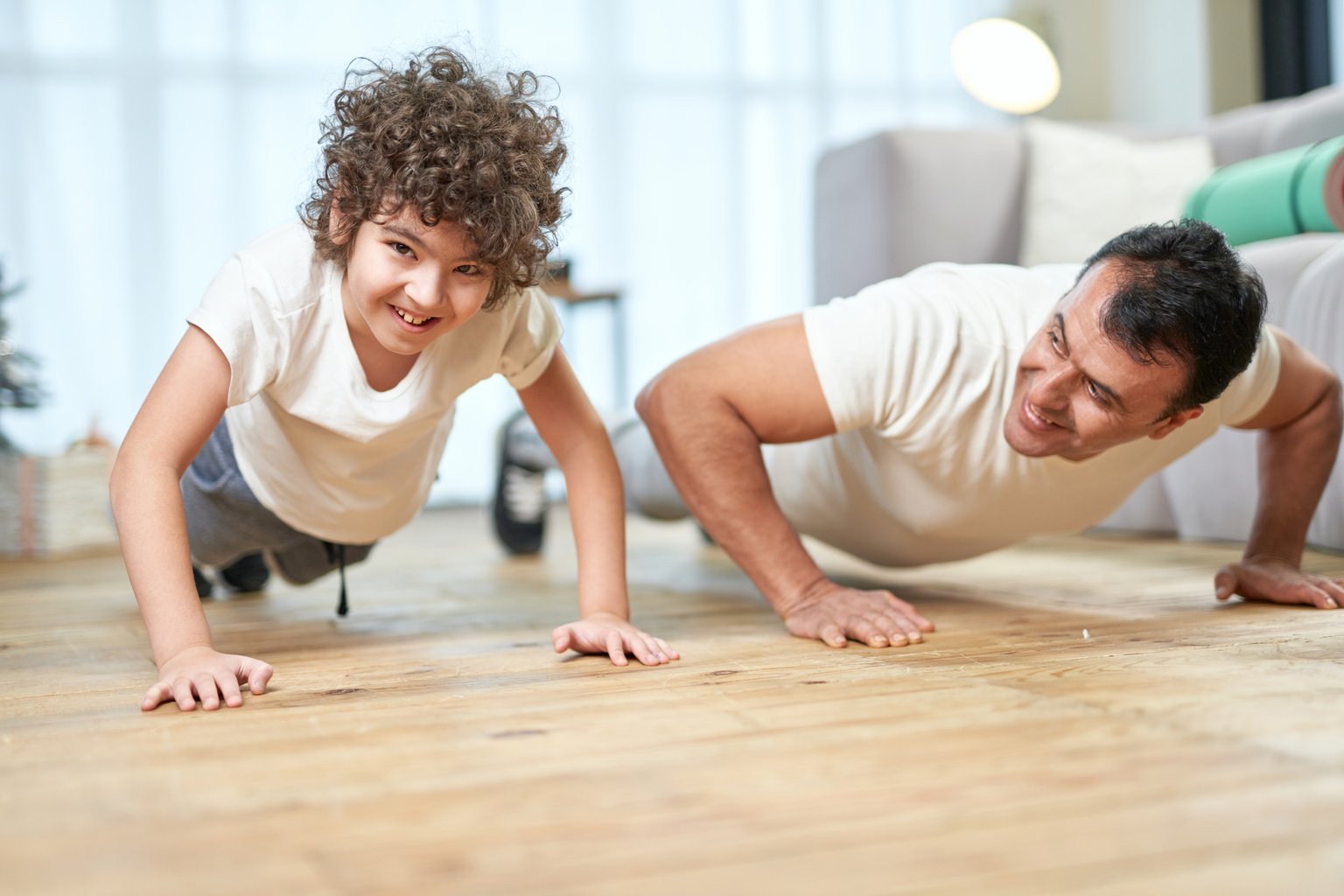 A parent and child doing push-ups together at home, smiling