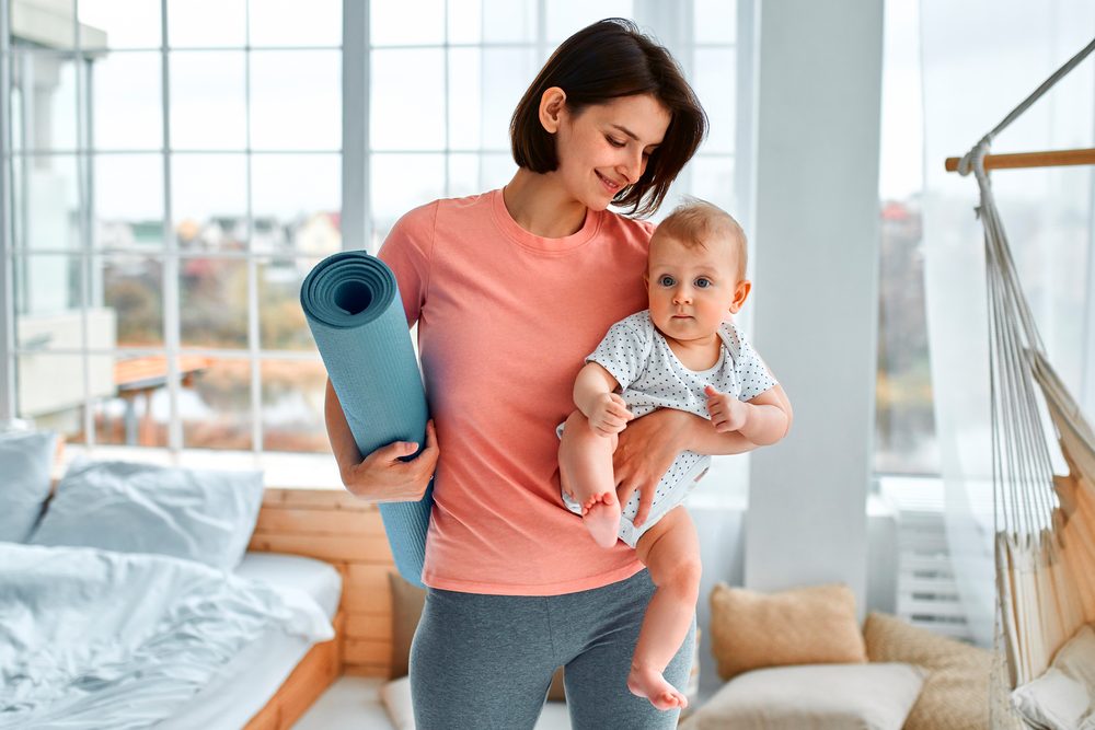 A parent exercising at home while holding a young child