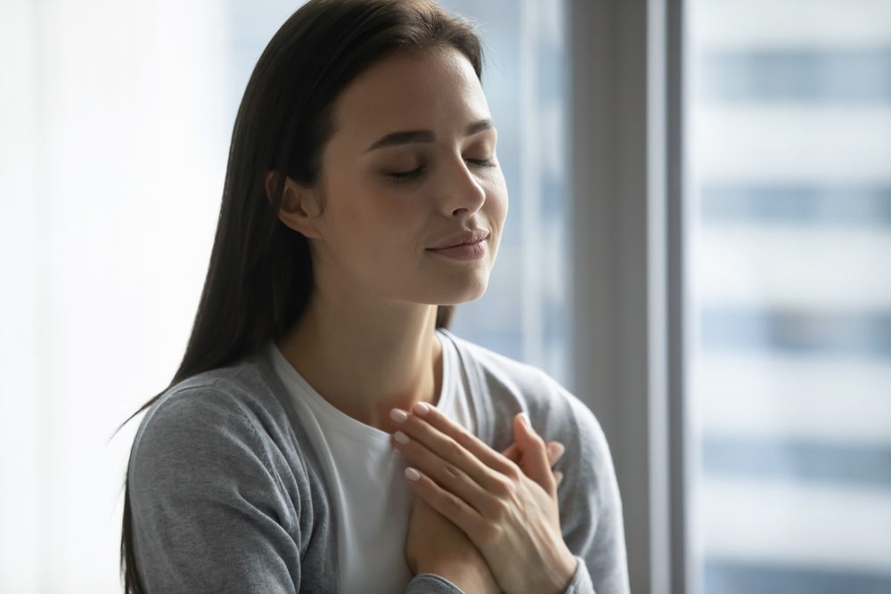 A woman with her hands over her heart, a gesture of self-compassion