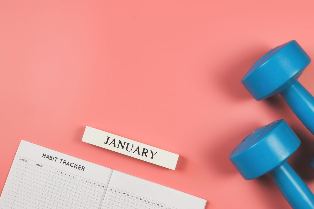 A habit tracker, calendar, and dumbbells, representing a simple weekly training plan