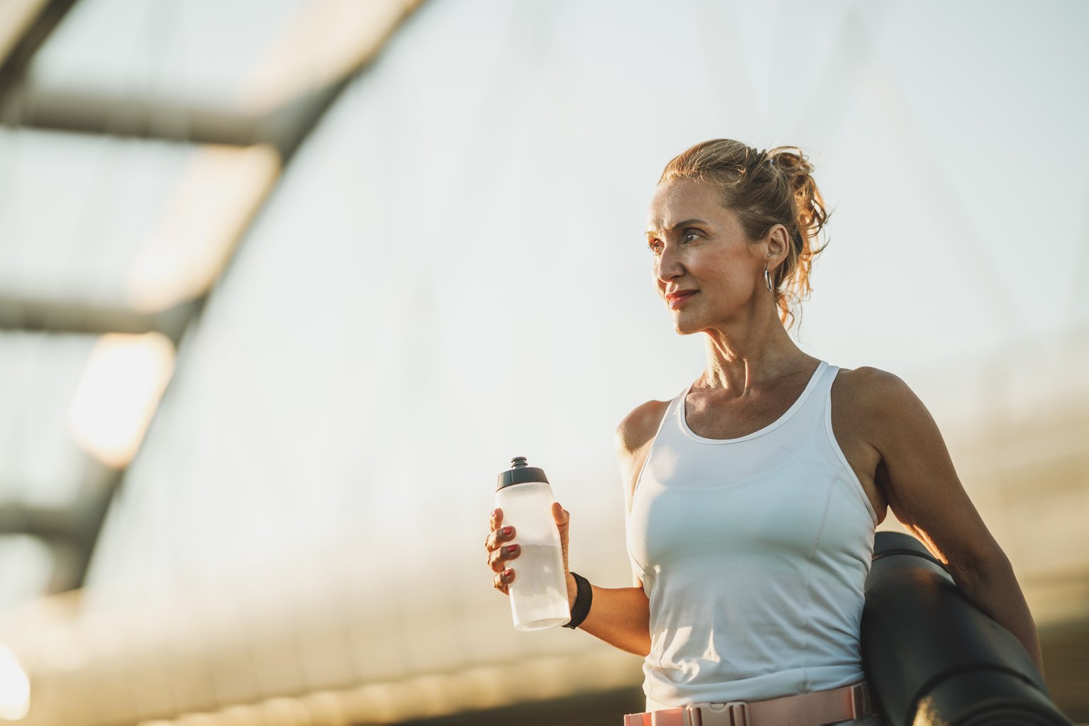 A woman walking outdoors on a bridge, relaxed and holding a water bottle