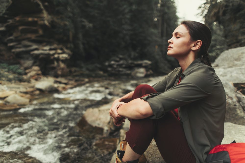 A woman resting peacefully outdoors near a river after a gentle walk