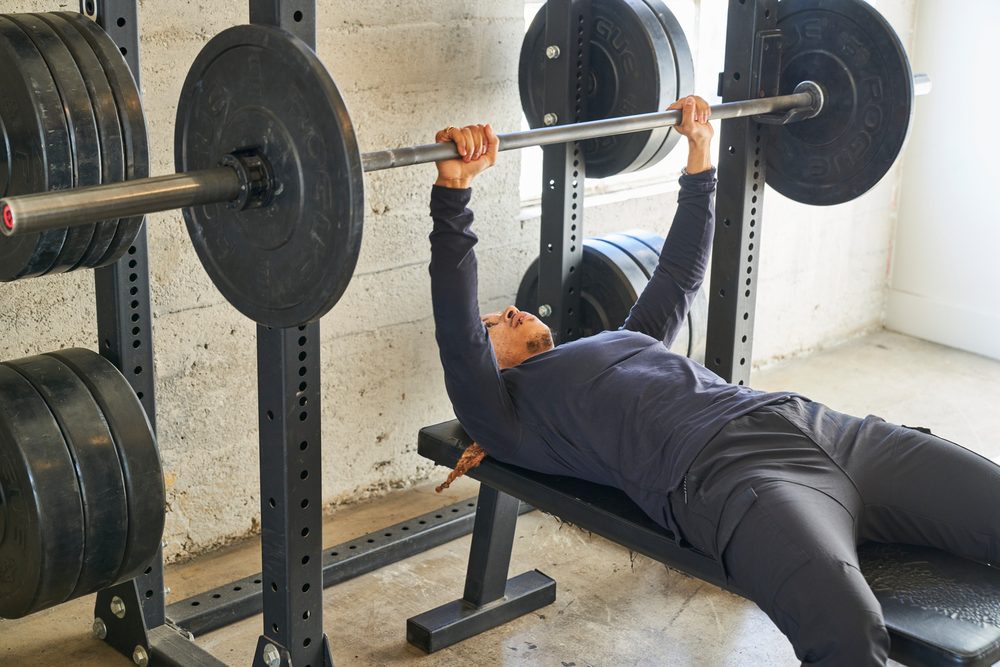 A man bench pressing with a barbell inside a squat rack with safety bars set