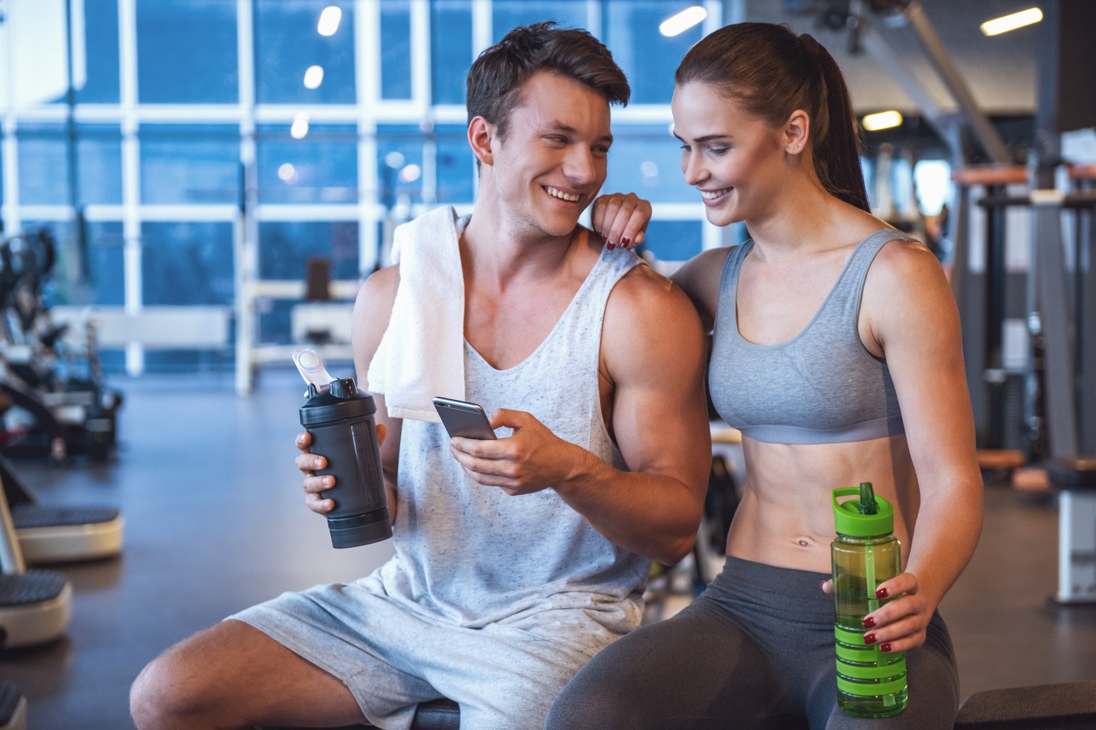A smiling couple checking a workout on a phone together during a rest break at the gym