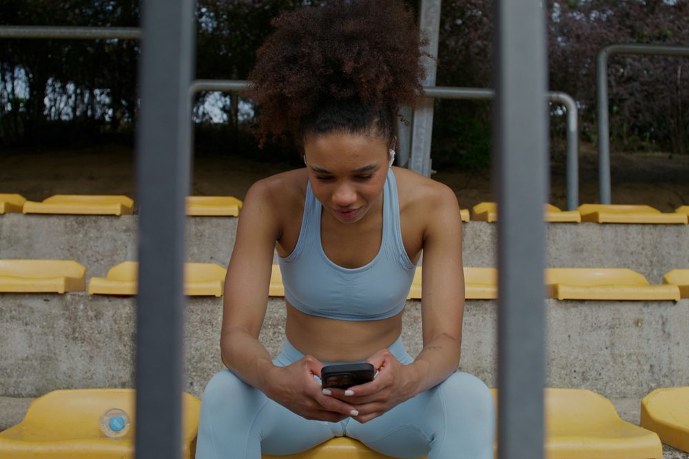 A woman checking her phone on bleacher seating, taking a moment during her workout