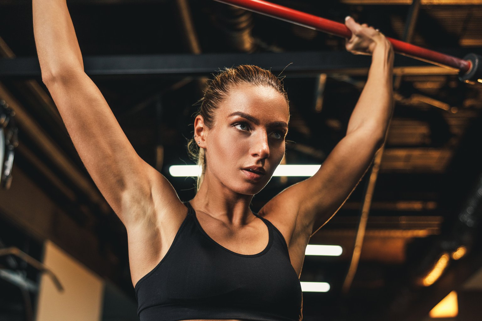 A woman performing a controlled overhead shoulder exercise in the gym