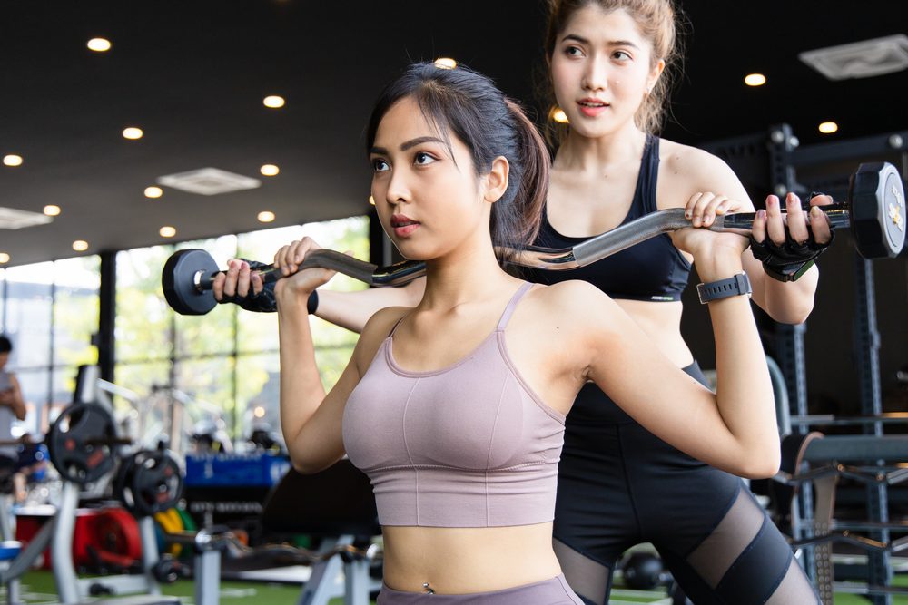 Two women training together in the gym with barbells