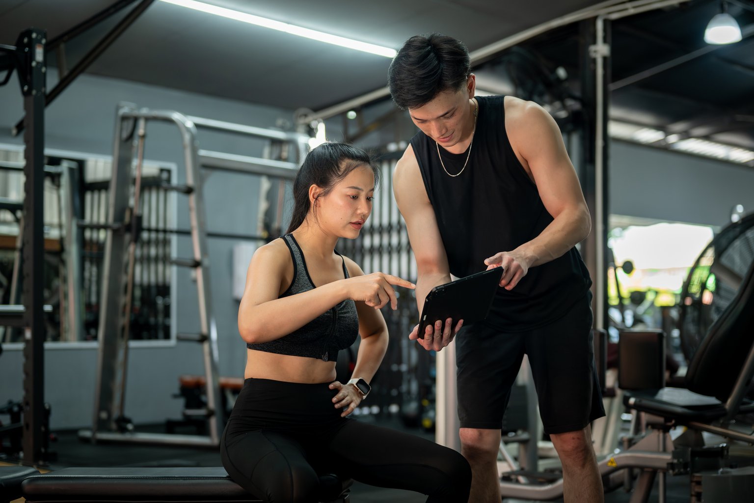 A woman discussing her workout program with a fitness trainer at the gym