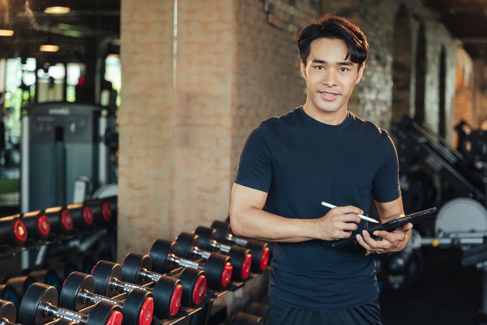 A gym trainer holding a tablet, ready to answer a member's question