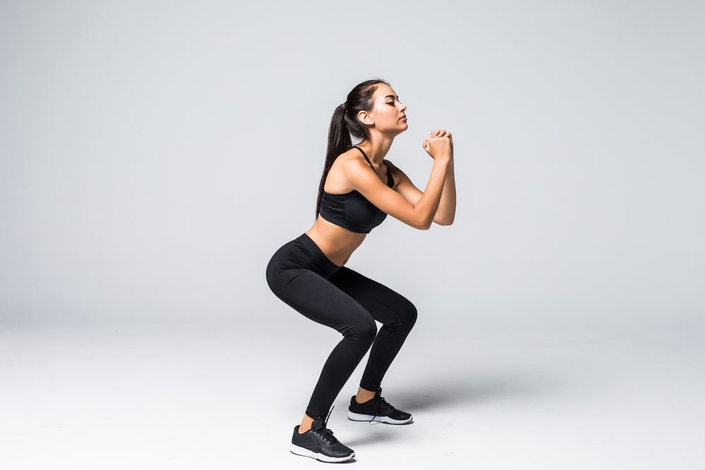 A woman practicing a bodyweight squat with her hands clasped in front of her chest