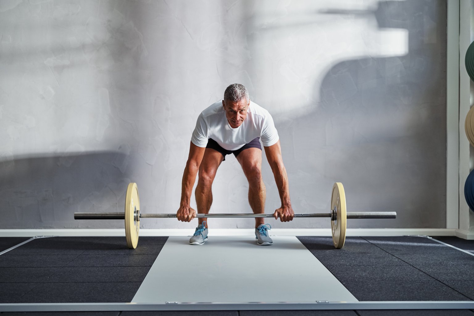 A man training alone in an empty gym, lifting a barbell with focus