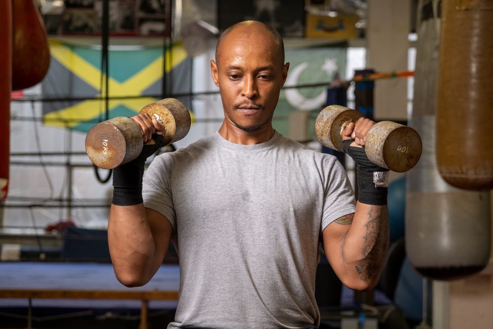 A man in a gym lifting dumbbells on his own, focused on his workout