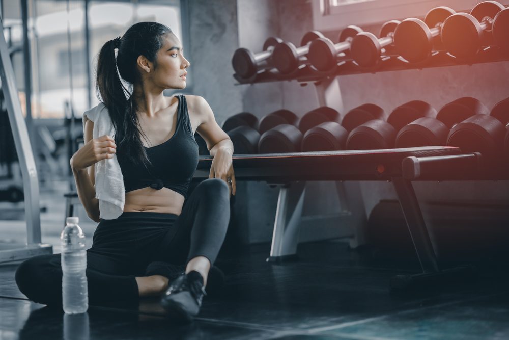 A woman sitting and resting on the gym floor between sets