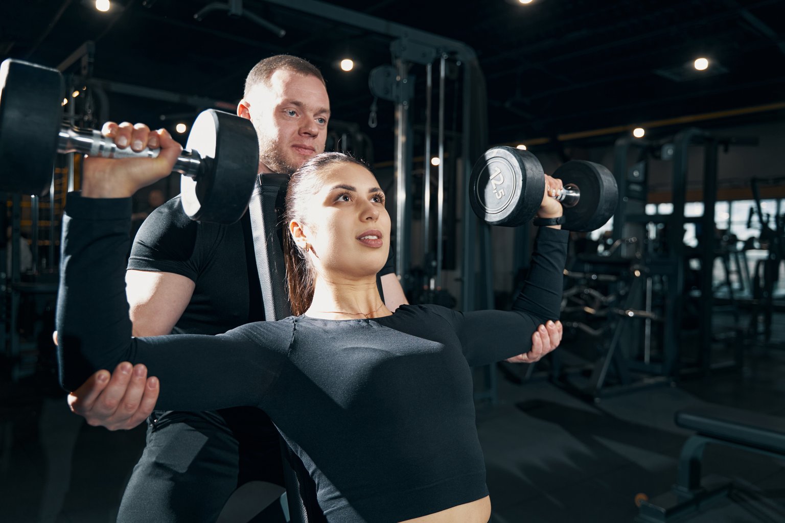 A woman performing a seated shoulder press with controlled form in the gym