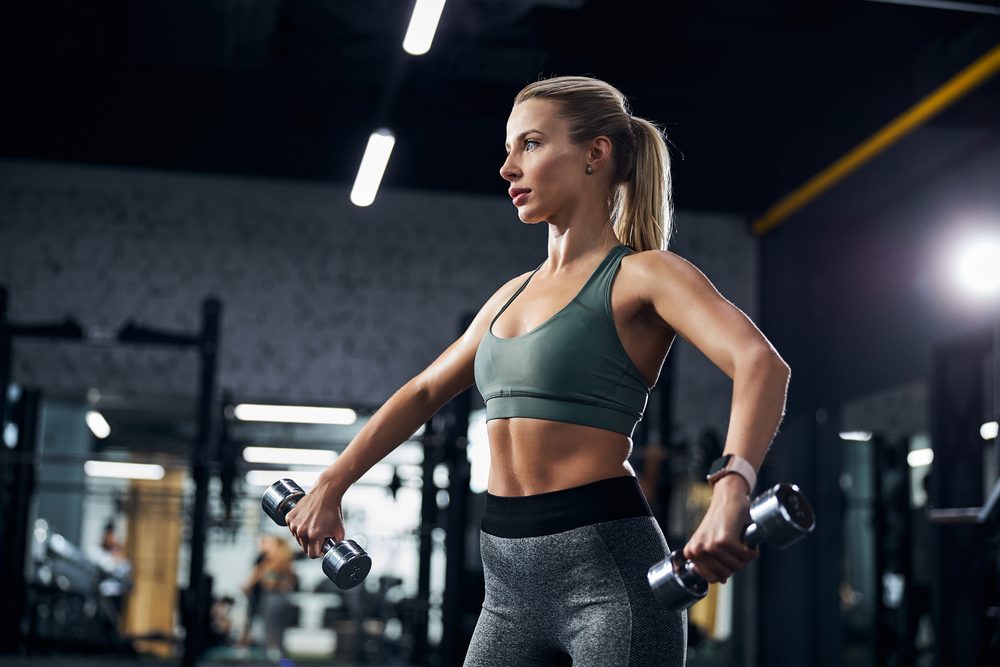A woman performing a lateral raise with dumbbells, arms extended to the side