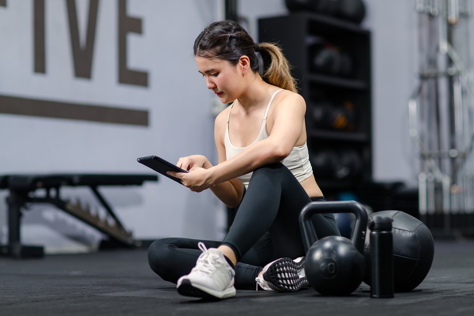 A woman sitting on the gym floor checking her phone between sets