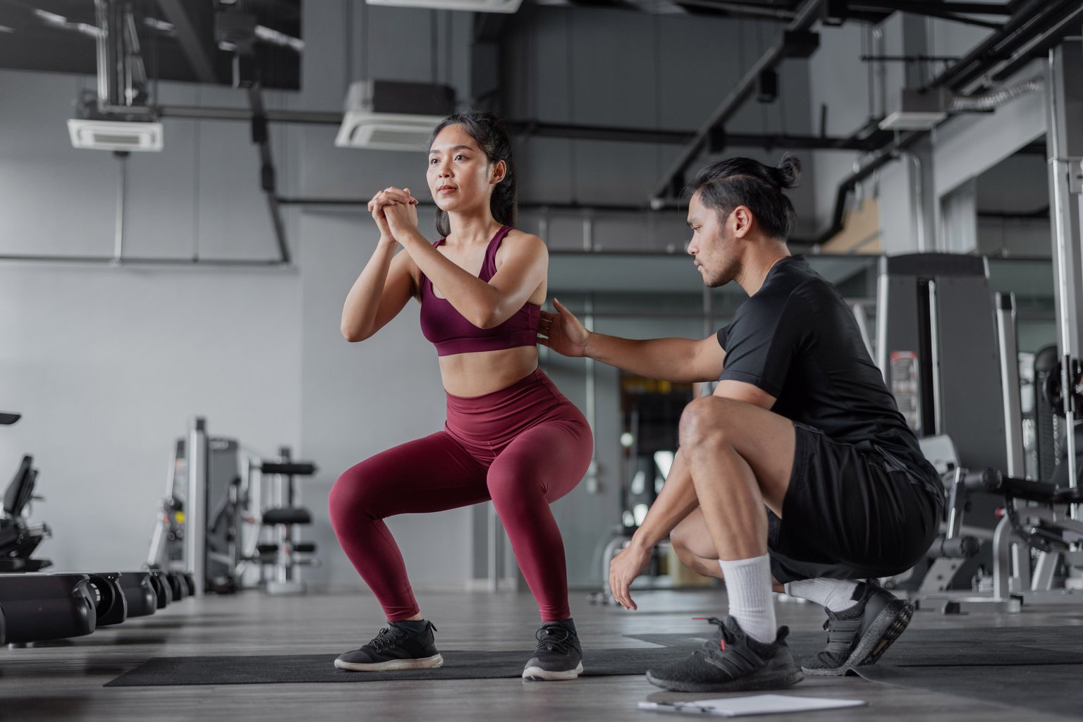 A trainer helping a woman practice a squat with careful form in the gym
