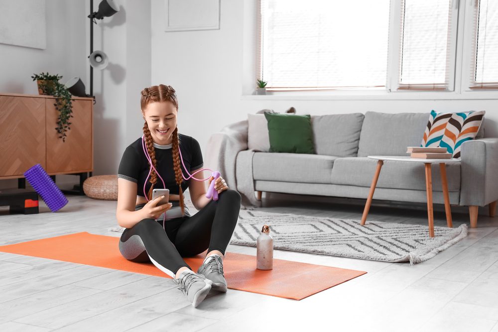 A person sitting on a yoga mat checking their phone, managing limited time before a workout