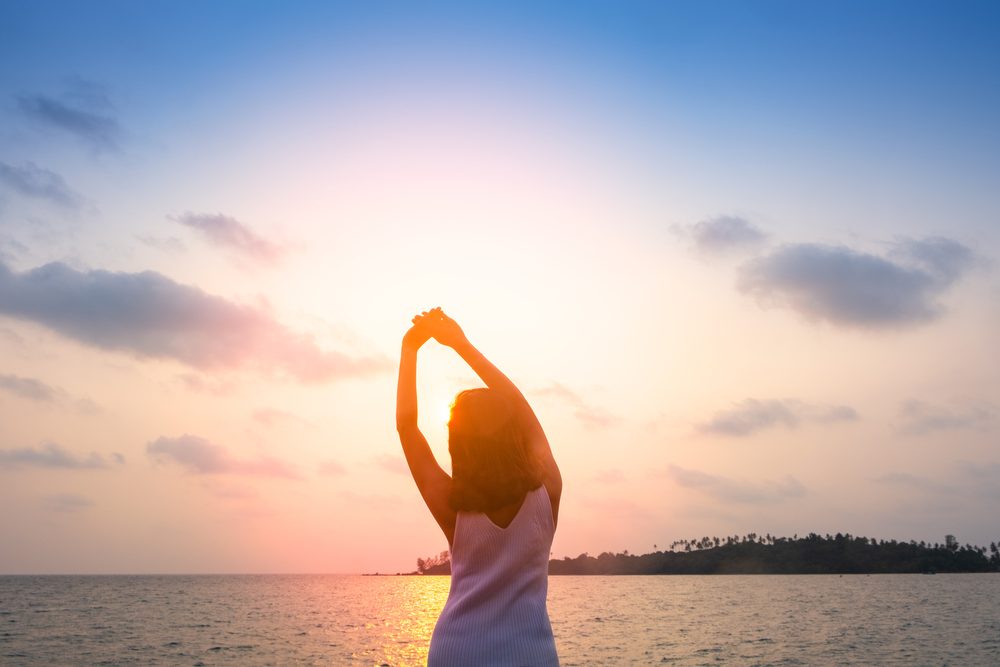 A woman stretching her arms overhead in the early morning sunlight