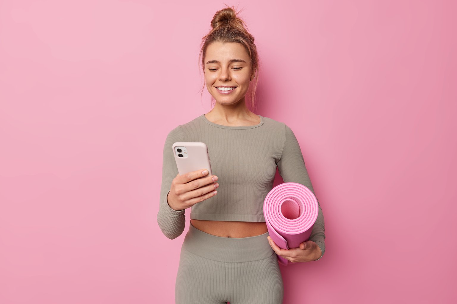 A woman holding a phone and a rolled fitness mat, ready to start her first workout