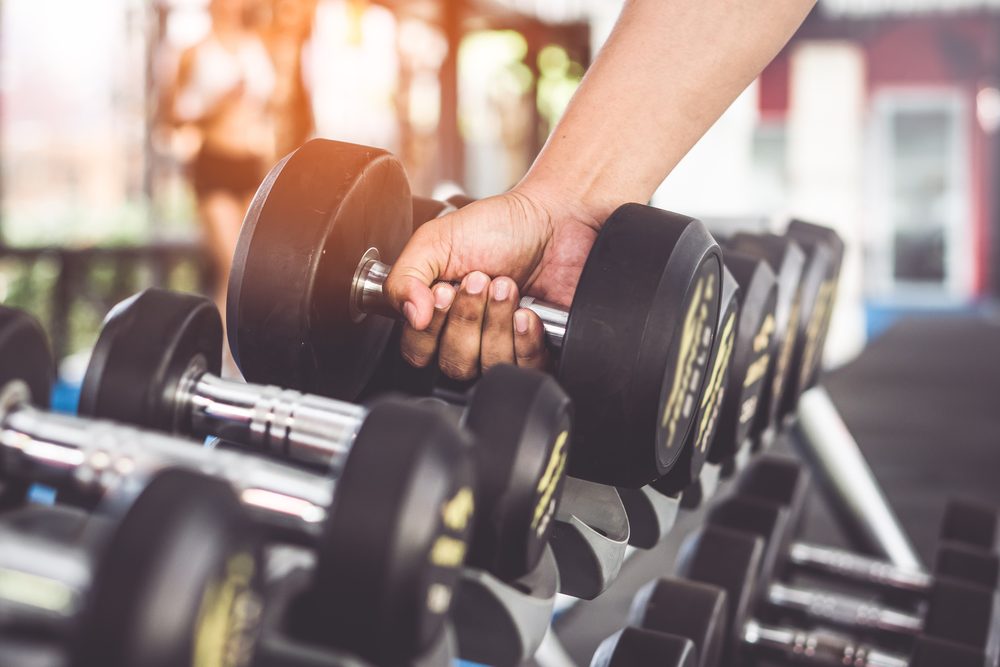 A hand reaching for a dumbbell on a gym rack, choosing equipment for the next exercise