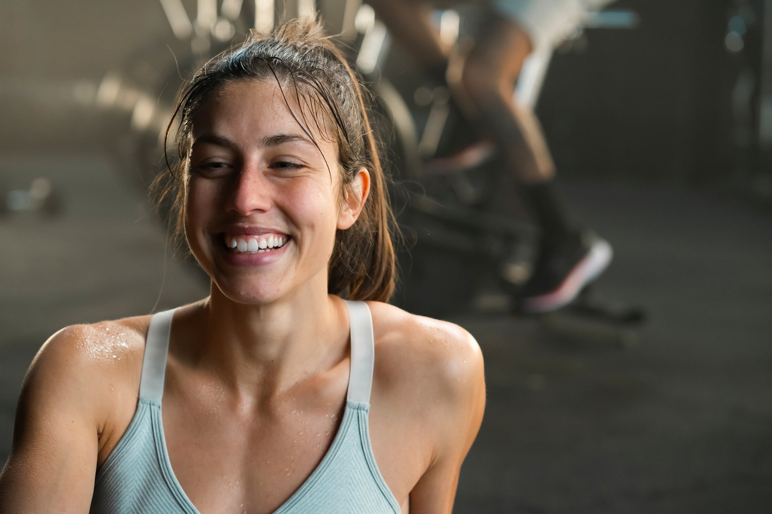 A woman smiling and relaxed after a workout, sitting on the gym floor