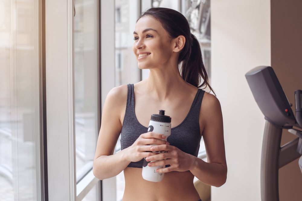 A woman holding a water bottle, calm and composed after training