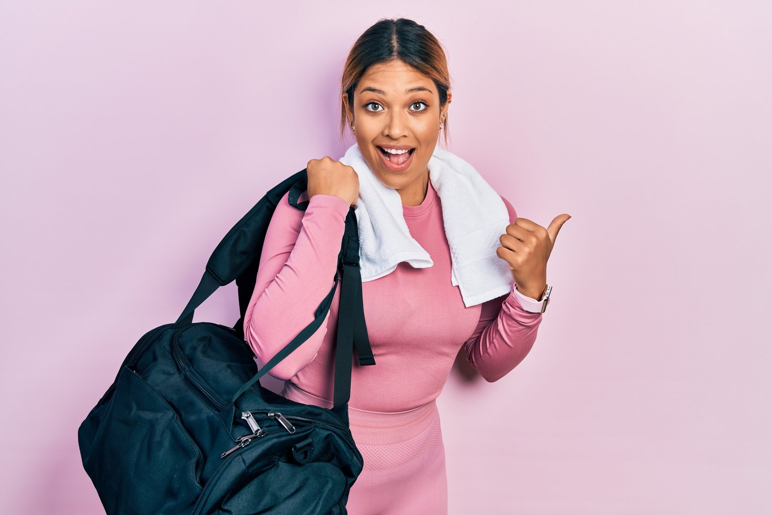 A smiling woman holding a gym bag and towel, ready and confident to train
